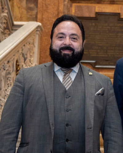 Luis Redondo, President of the National Congress of Honduras, a bearded man wearing a brown suit with a vest and tie, stands in front of an ornate marble staircase in a historic building