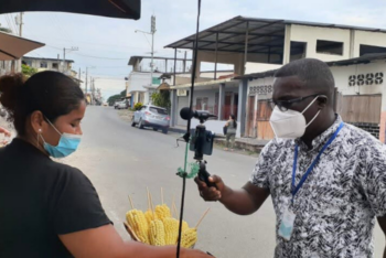 A reporter interviews a street vendor selling corn on a quiet street in a small Ecuadorian town.
