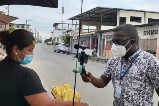 A reporter interviews a street vendor selling corn on a quiet street in a small Ecuadorian town.