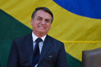 Jair Bolsonaro smiles during a ceremony with the Brazilian flag in the background