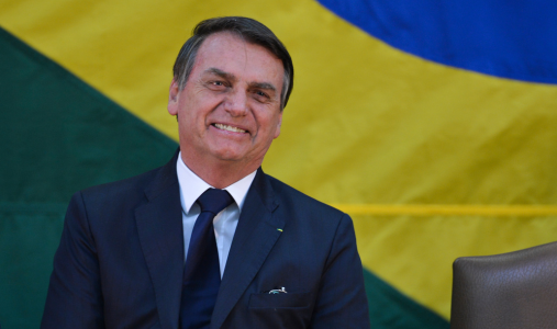 Jair Bolsonaro smiles during a ceremony with the Brazilian flag in the background