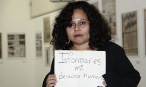 Woman looking at the came with a poster that says "To inform is my human right"
