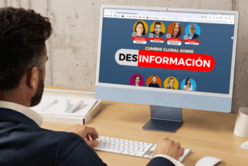 A man looks at a computer screen displaying some of the panelists of the Global Summit on Disinformation.