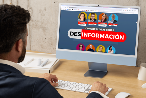 A man looks at a computer screen displaying some of the panelists of the Global Summit on Disinformation.