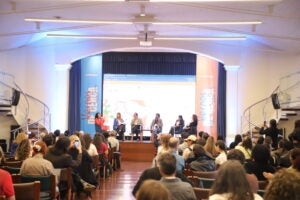 Auditorio en el que se ven seis personas sentadas presentando ante un público.