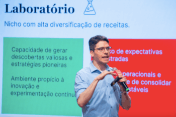 Guilherme Fowler, coordinator of the News Tech study, speaks on stage holding a microphone. Behind him, a presentation slide reads “Laboratory — Niche with high revenue diversification,” with text about innovation and experimentation.