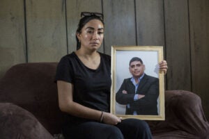 Woman sitting in a couch dress in black holding the picture of her murdered husband.