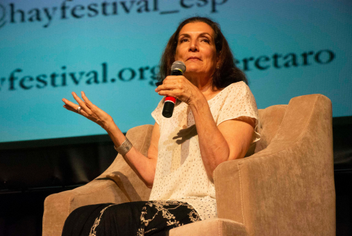 Woman with microphone in hand seated in chair in front of screen