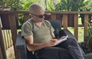 Belgian journalist Arthur Debruyne taking notes in a notebook, seated on a chair in a terrace. (Photo: