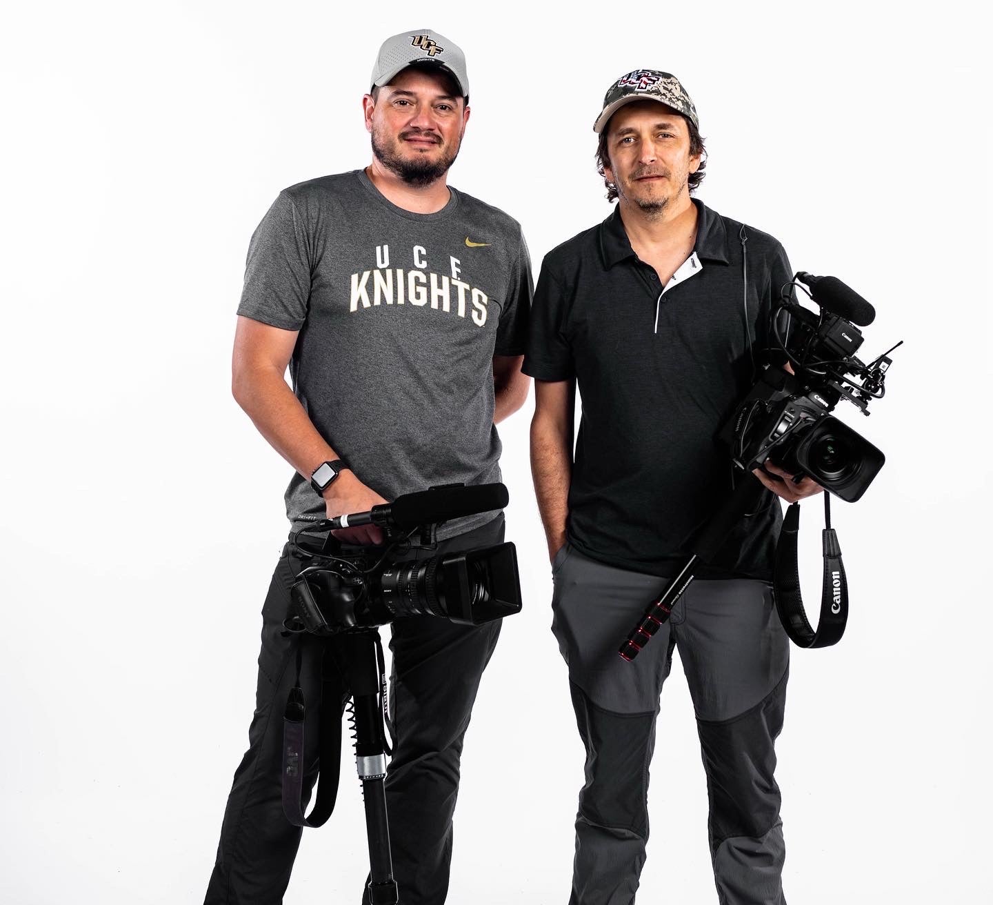 Two men smiling holding video cameras looking at the camera