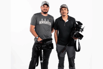 Two men smiling holding video cameras looking at the camera