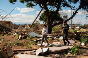Man and woman walk through destroyed houses and trees