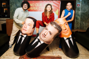 Un hombre y dos mujeres posan sosteniendo figuras inflables gigantes de Elon Musk, Mark Zuckerberg y Jeff Bezos.